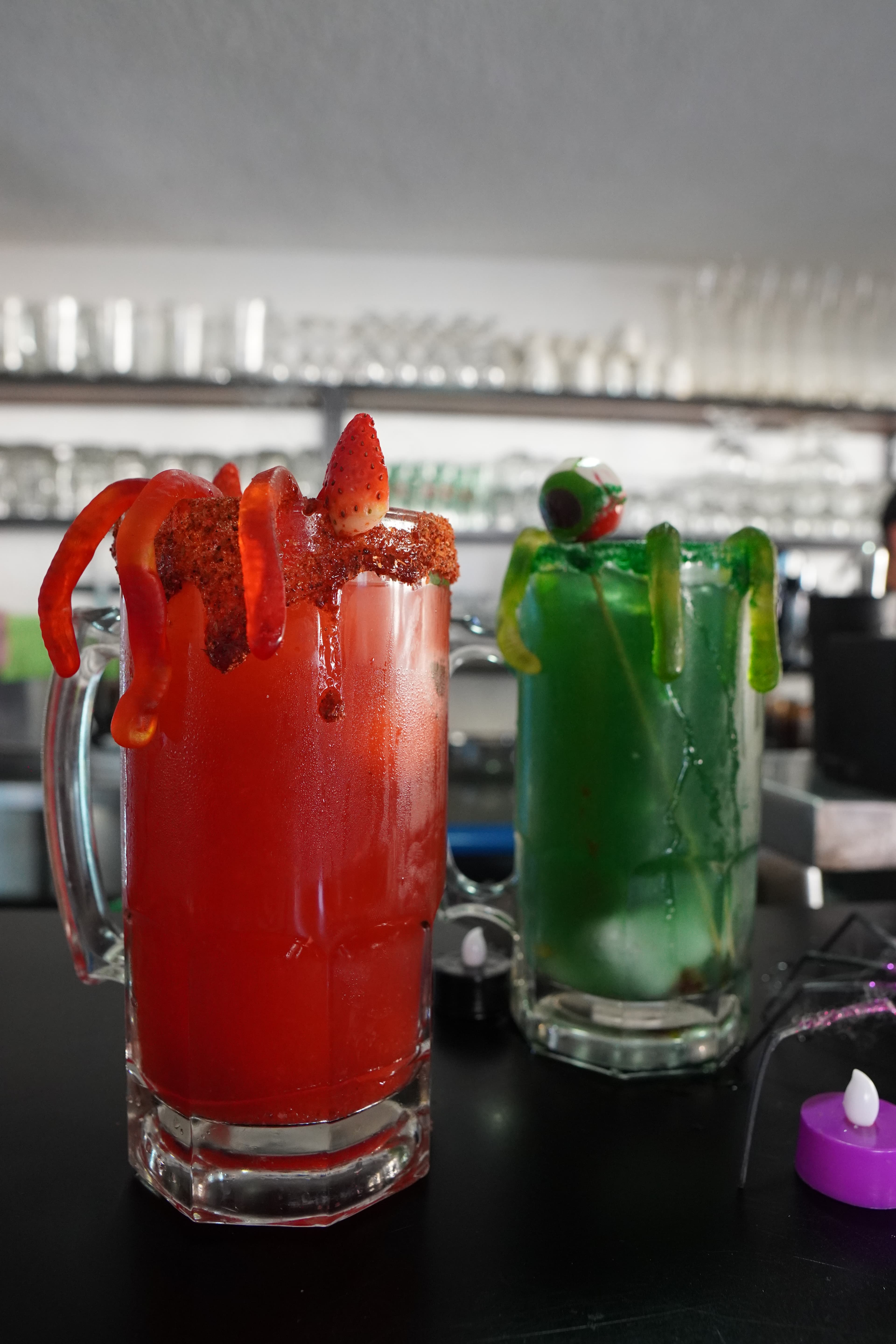 A close-up of a blue cocktail with a lime garnish, glowing under blue light.